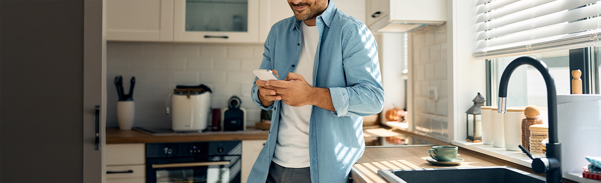 Man using smartphone in modern kitchen with black faucet and sink.
